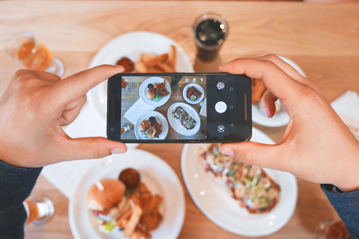 Hand holding phone and taking picture of their food